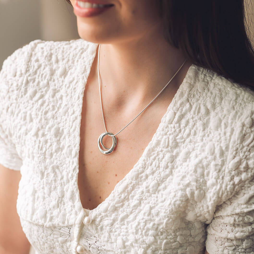 Woman wearing a textured white top with a silver necklace featuring two interlocking rings.
